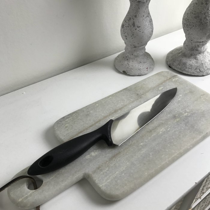Ett nyslipat knivblad ligger på en grå slipsten vid en vit bänk med två grå kandelabrar i bakgrunden.