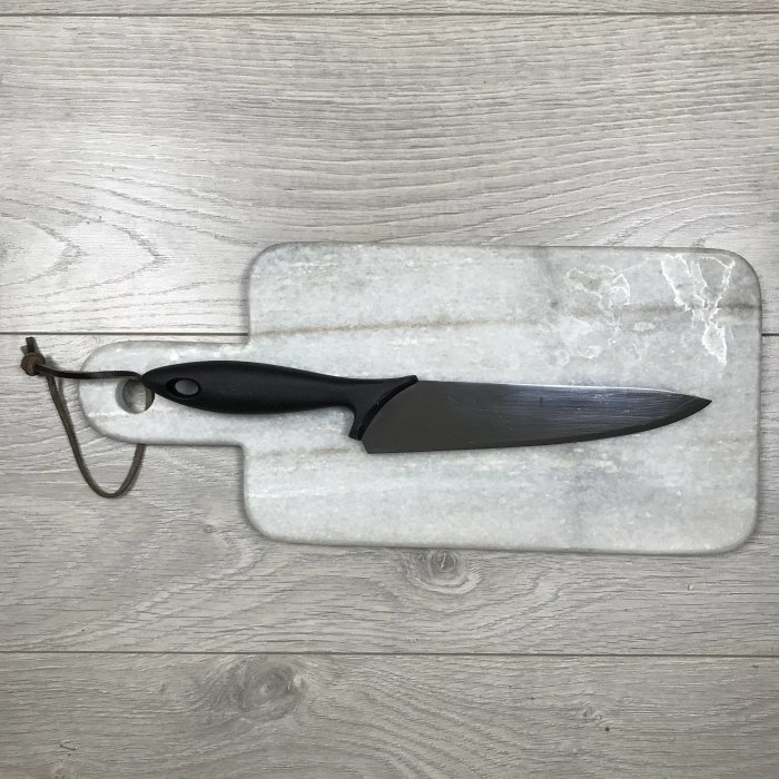 Svart kniv med slät svart handtag ligger på en marmorbricka mot ljust trägolv.