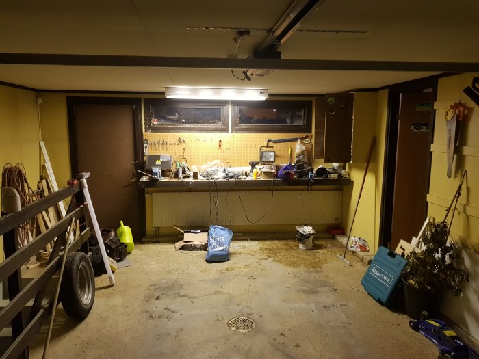 Ett oorganiserat garage före storstädning med verktyg och material utspritt på arbetsbänken och golvet.