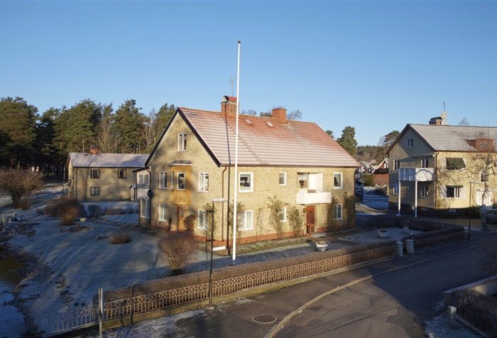 Tvåvåningshus med tegeltak och tre lägenheter, snötäckt trädgård och angränsande gata i bostadsområde.