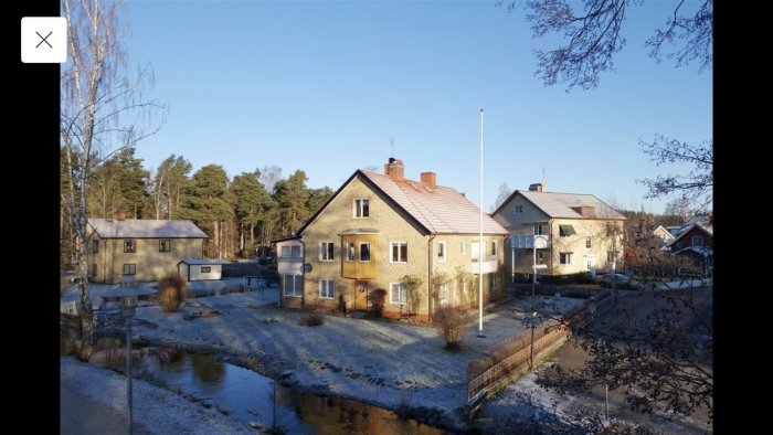 Tvåvåningshus med stenfasad, omgiven av en snöbelagd trädgård och barträd, potentiell renoveringsprojektbostad.