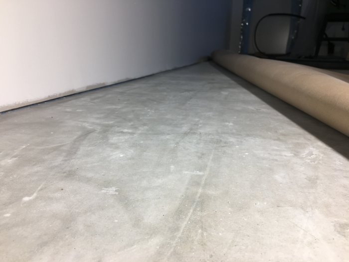 Ett nyslipat betonggolv utan synliga ojämnheter längs en vit vägg med rulle på golvet.