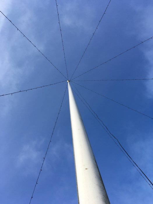 Vy uppåt längs en flaggstång med strängar av ljus mot en klarblå himmel.