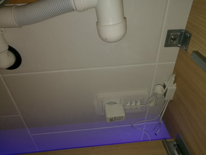 En köksbänk med en installerad blå LED-strip under och en synlig sensor kopplad till ett eluttag.