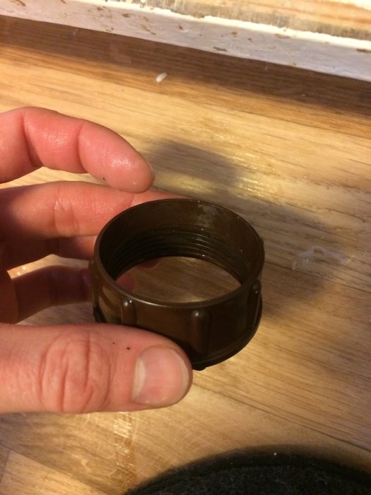 Hand håller en brun plastkoppling utan synlig packning mot träbakgrund.