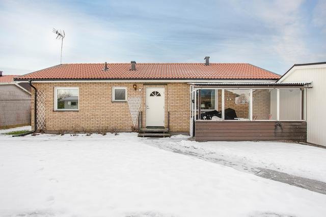 Enfamiljshus i tegel med snötäckt trädgård och anslutande byggnad under vinter.