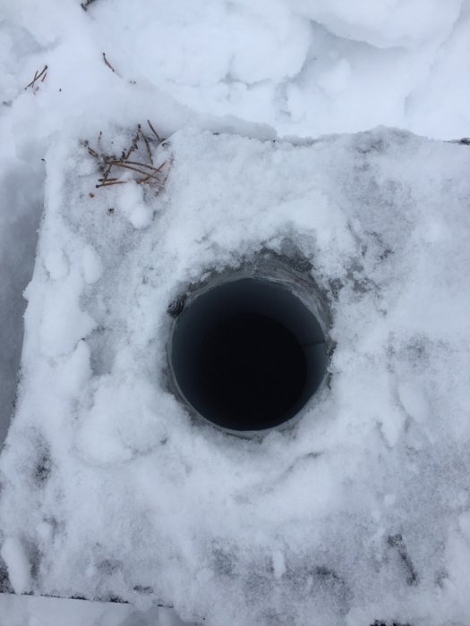 En öppen cirkulär ventilationstrumma i snötäckt tak.