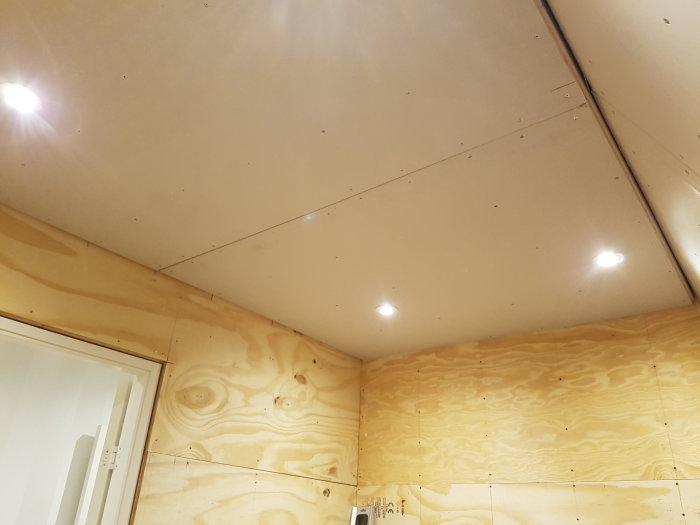 Tak med nyinstallerat gipsskivor och infällda spotlights, väggar klädda i plywood.