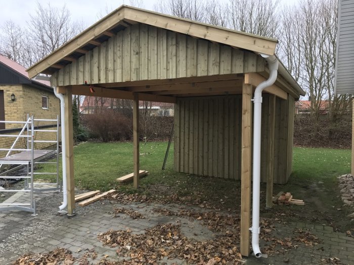 Obyggd träcarport med uppsatt panel och regnstuprör, arbetsmaterial syns på marken.