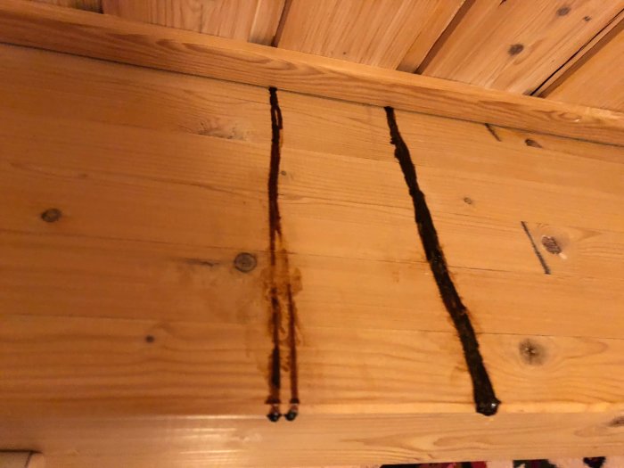 Brunsvarta sega läckage ränder på ljus trävägg i en uppvärmd stuga, liknar kåda men luktar skog.