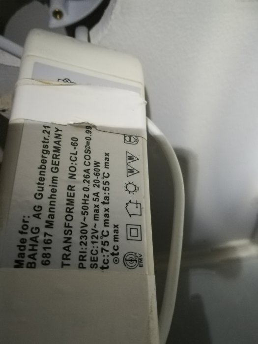 Närbild av en transformator med specifikationer, anslutna kablar och vägguttag i bakgrunden.