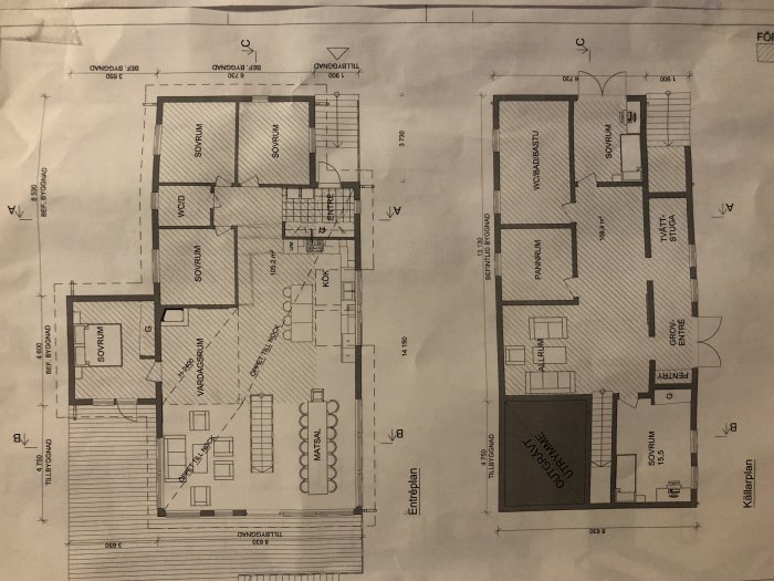 Skrynklad byggritning av ett hus med markerade källarrum och planerad utbyggnad, inklusive golvvärme och bergutsprängning.