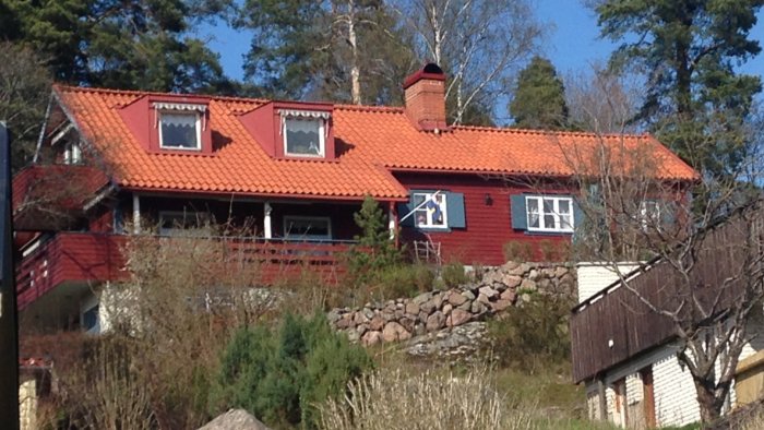 Röd svensk villa med takkupor och en låg altan på baksidan som planeras att byggas in.