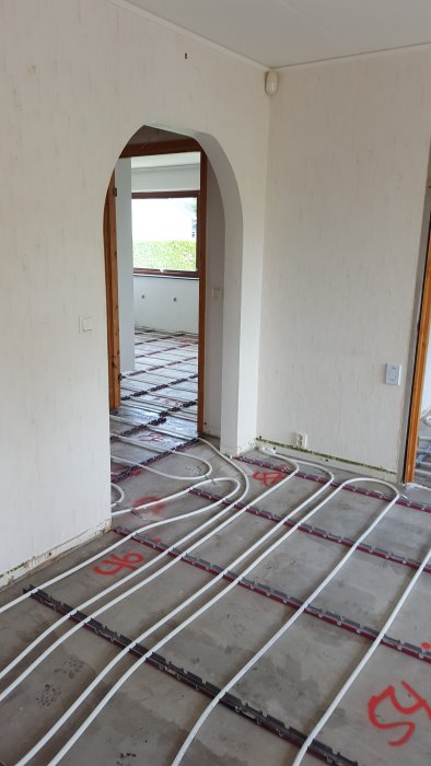 Installation av vattenburen golvvärme i ett hus under renovering, synliga värmeslingor på betonggolv.