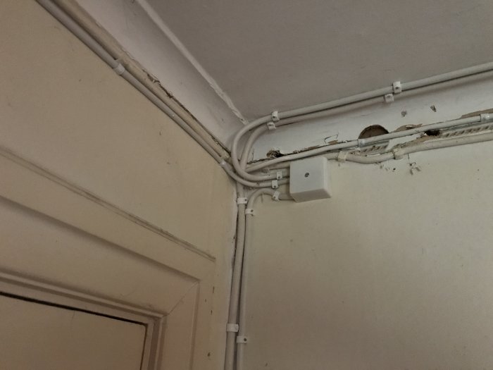 Gamla kablar och elinstallationer på en vägg i ett hörn ovanför en dörrkarm.