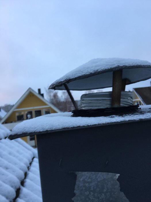 Takhuven med snö och synligt flexrör samt tecken på möjligt vattenintrång med gult hus i bakgrunden.