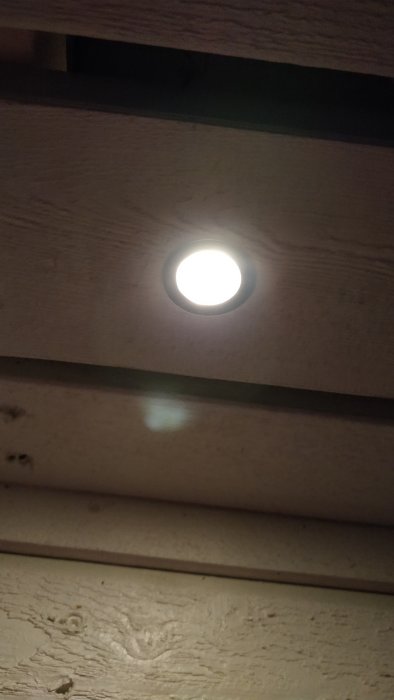 LED-spot inbyggd i trall med träribbor ovanför, tänd och lyser upp området.