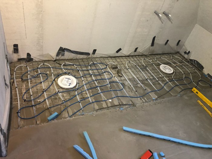 Pågående byggprojekt med två golvbrunnar, installerad golvvärme och förberett för flytspackling.
