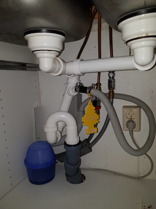 Vy under en köksbänk som visar rör och kopplingar för en vask, inklusive avlopp och vattenledningar.