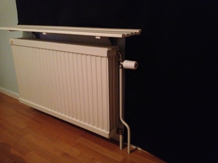 Fyr-radig radiator med termostat nära en altandörr i ett mörkt rum med parkettgolv.