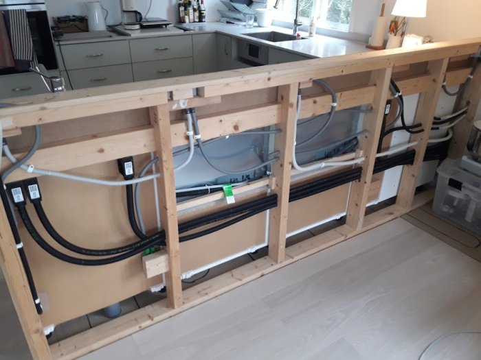 Kök i renovering med oskyltad köksö och synliga rör och elinstallationer under arbetsbänken.