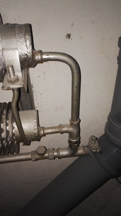 Gammalt upphängt värmeelement kopplat till rörledningar på en vit vägg i ett garage.