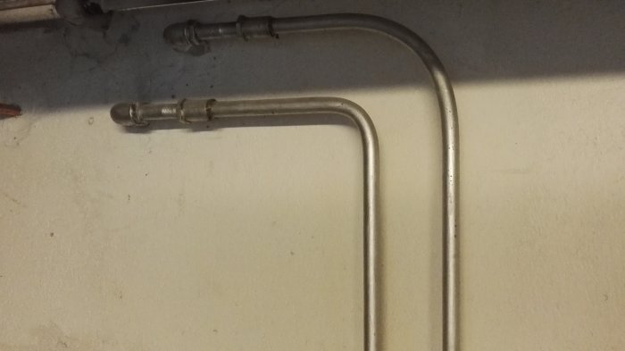 Väggmonterade vattenrör i metall ledande uppåt och böjda i 90-graders vinkel i ett garage.