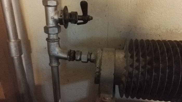 Gammalt metallradiatorselement med anslutande rör och ventiler i ett garage, behov av demontering.
