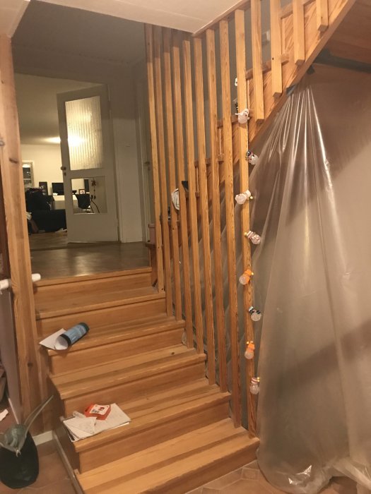 Trappa av furu delvis täckt med plast, med räcke och steg synliga, färg och pensel på ett steg.