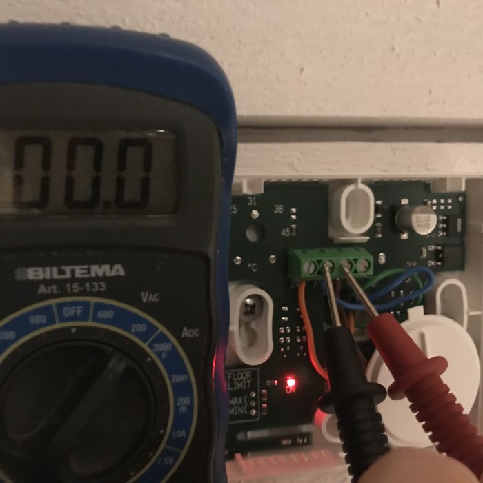 Multimeter visar 0.0V med testspetsar anslutna till termostat, röd lampa på kopplingslåda tänd.