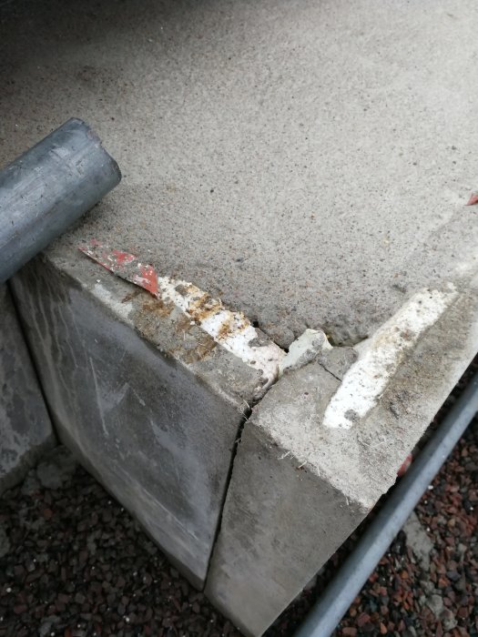 Betonggrund med framstickande isolering och en sönderfrasad kant, möjlig ingjuten plast synlig.