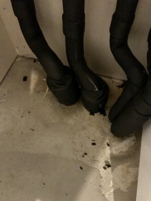 Isolerade rör med synliga blöta fläckar och en fuktig ring på betongplattan.