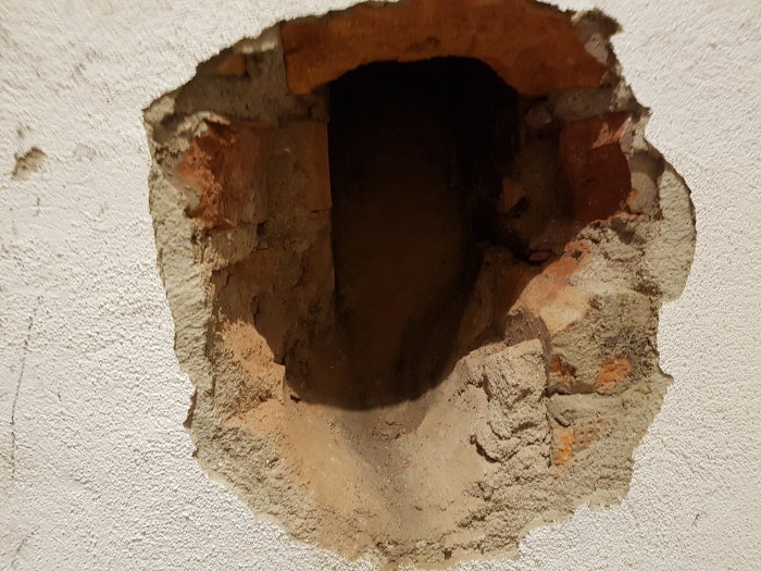 Ett hål i en vit vägg med tegelstenar som leder till ett mörkt utrymme utan öppning.