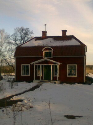 Röd tegelvilla med gröna knutar och snö på marken, firar 100 år, där ägaren önskar nytt handfat.