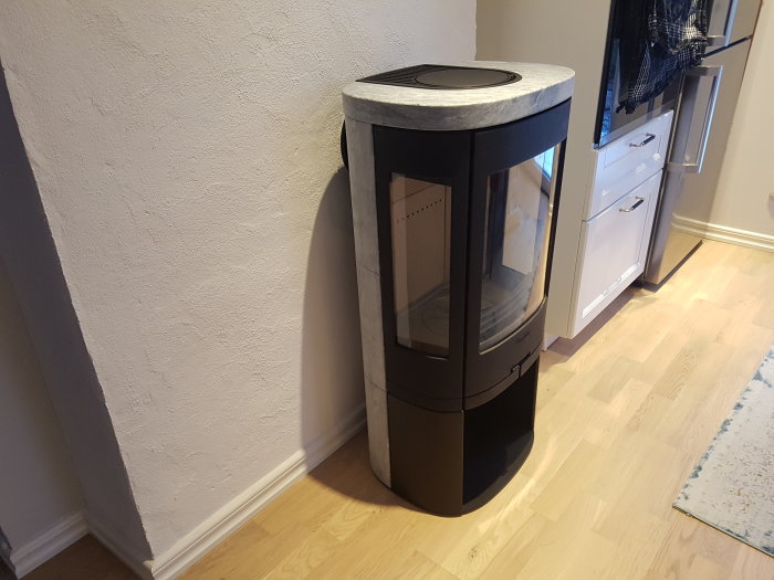 Modernt svart kamin med glasdörr installerad i ett hörn bredvid vita köksskåp.