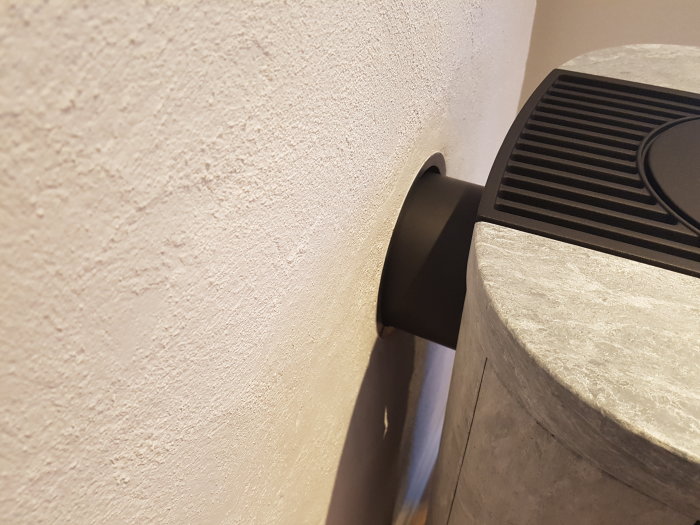 Närbild på en nyinstallad kamin med synlig stenbeklädnad och rökrör mot putsad vägg.