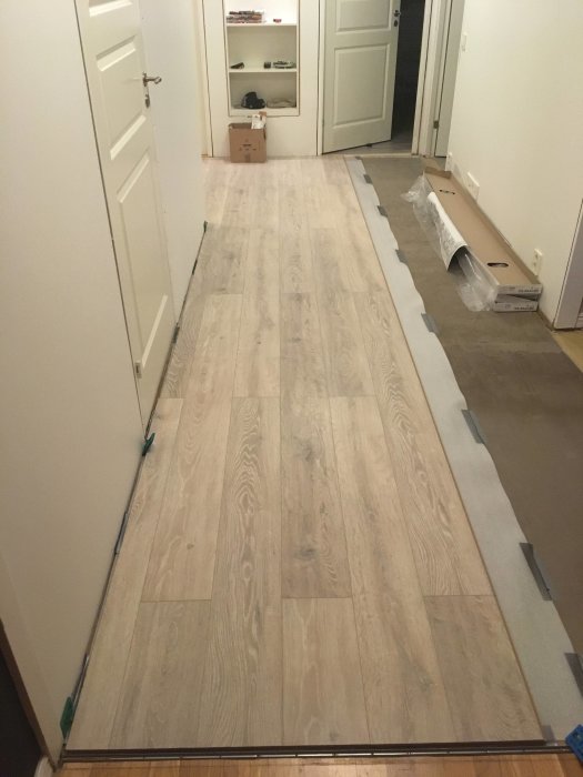 Nyinstallerat ljust laminatgolv i en korridor med dörrar och ouppackade golvpaket.