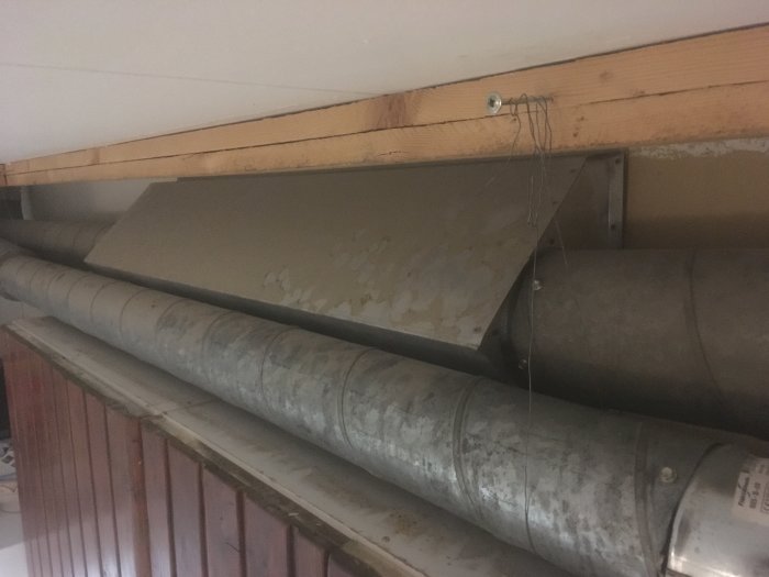 Metallrör för ventilation och en grå plåtlåda monterade under köksskåpen i ett renoveringsprojekt.