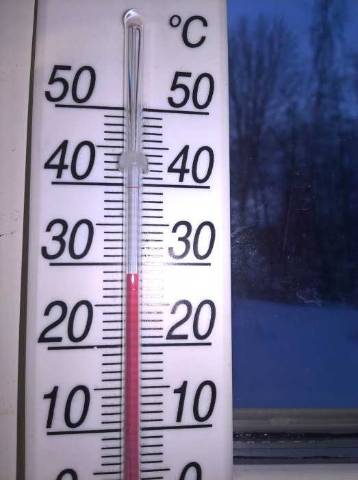 Termometer inomhus visar +15 grader Celsius med utsikt över ett kallt, mörkt vinterlandskap.