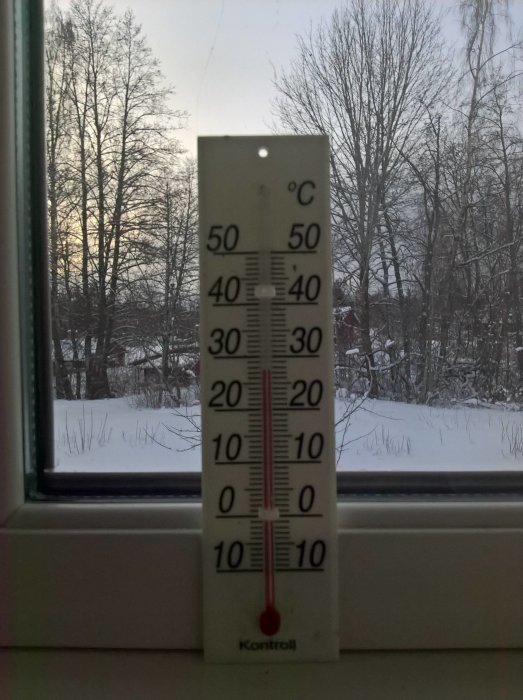 Termometer vid fönster visar +15 grader inomhus, snötäckt landskap utanför.