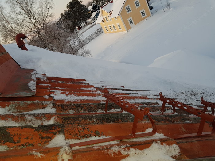 Stegstöd på röda tegelpannor med bakgrund av ett gult hus och snölandskap.