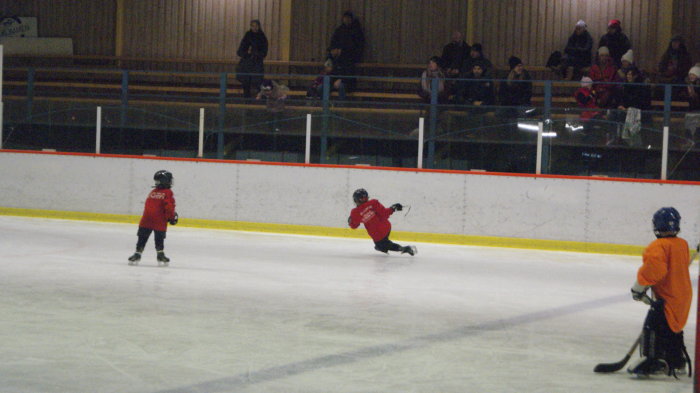 Barn i röd tröja gör målgest på ishockeyplan medan publik tittar på.