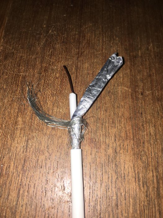 En skadad antennkabel med blottad inre ledare och splittrad skärmning på ett träbord.
