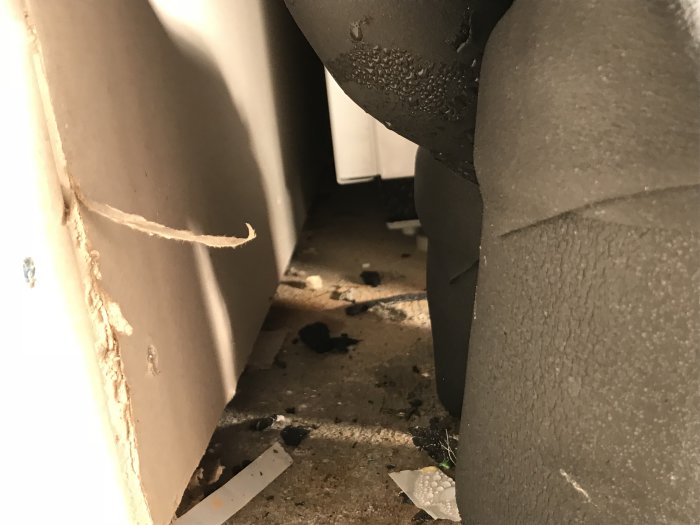 Blöt skada och limrester i ett hörn mellan golv och vägg med synliga droppar och spillt material.