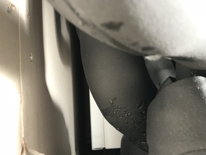 Närbild av fuktiga områden på en svart yta, troligen relaterat till byggproblem med lim.