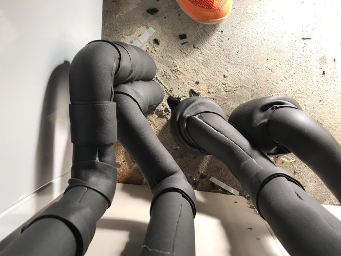 Svarta isolerade rörledningar med synliga limfogar och fukt, samt en orange hink i bakgrunden.