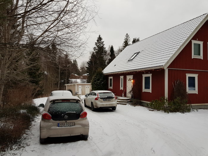 Röd husgavel med dörr och fönster på en snöig tomt, föreslagen utbyggnadsplats till höger om dörren.