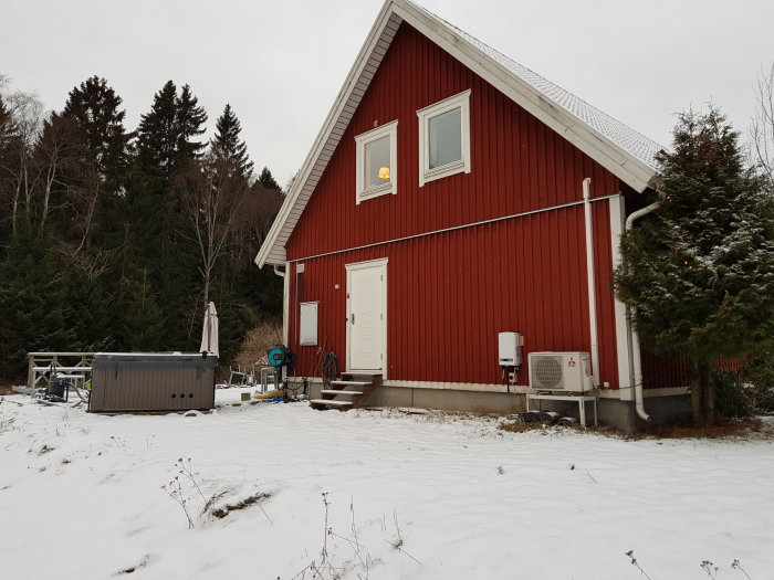 Östra gaveln på ett rött hus med en dörr och fönster, planerat för en utbyggnad till höger.