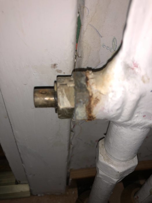 Rostig rördel där radiatoransluten till vägg, tecken på vattenläckage eller åldring.