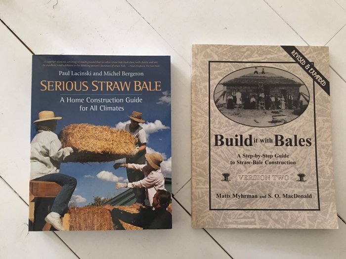 Två böcker om halmhusbygge, "Serious Straw Bale" och "Build It With Bales", på ett golv.